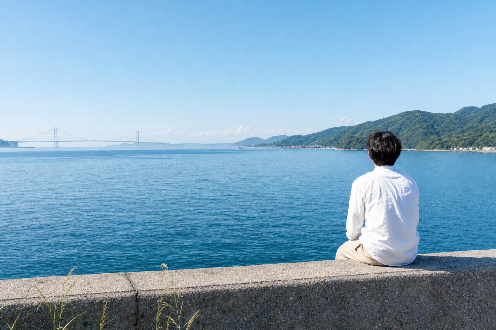 明石海峡大橋を望む淡路島の海辺。穏やかな光の中で海を眺める人物